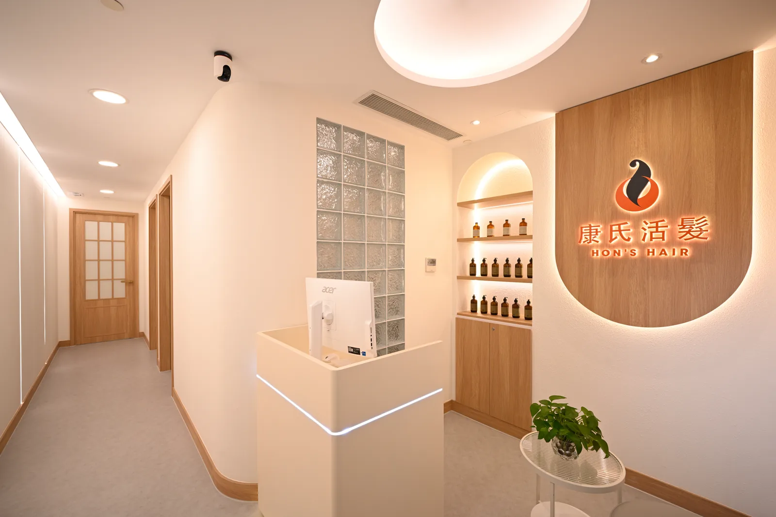 尖沙咀尊店接待處，暖木品牌牆寫著康氏活髮，旁為玻璃磚與通往護理房的通道